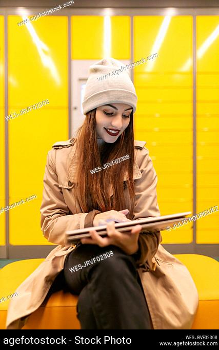 Woman using touch screen laptop sitting on couch in front of yellow wall