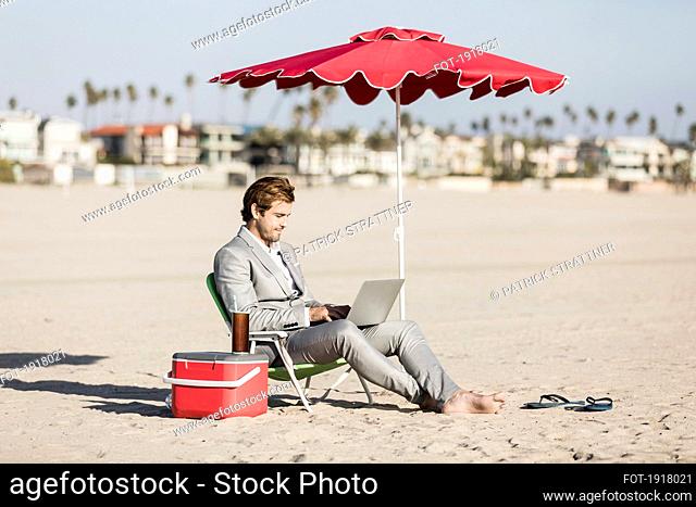 Barefoot businessman using laptop on sunny beach, Los Angeles, California