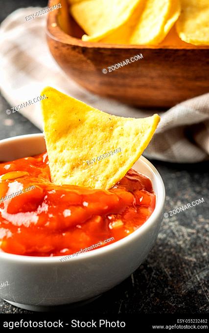 Corn nacho chips and tomato dip. Yellow tortilla chips and salsa on old kitchen table