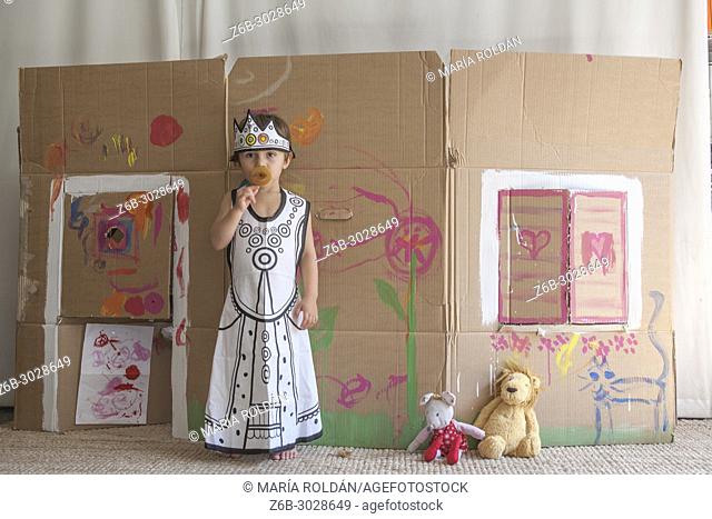 little girl dressed up as a queen in front of a painted carton house