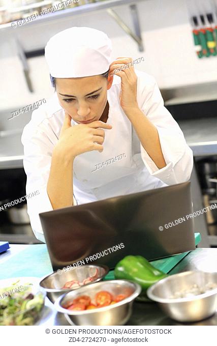 Pensive chef in restaurant kitchen with laptop computer