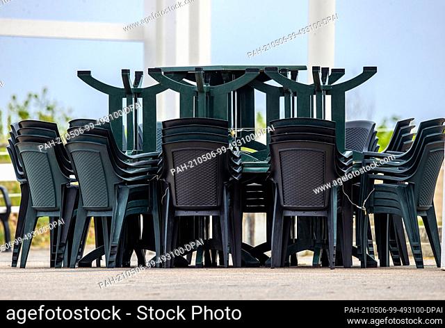 06 May 2021, Mecklenburg-Western Pomerania, Koserow: Stacked tables and chairs for outdoor gastronomy stand on the square at the pier