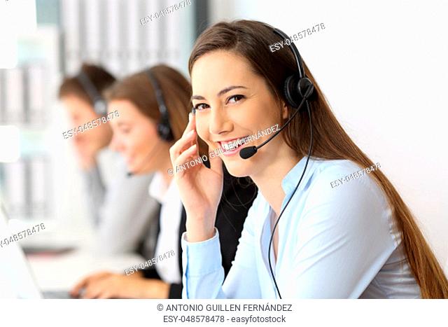 Happy telemarketer looking at you at office with other workers in the background