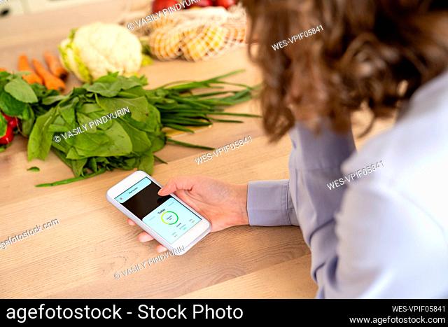 Woman using mobile app by vegetables at dining table