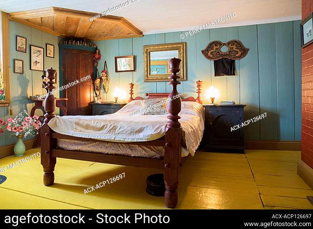 Irregular size wooden bed frame with sculpted bedposts in upstairs master bedroom with yellow painted wide plank floorboards inside an old 1835 Canadiana...