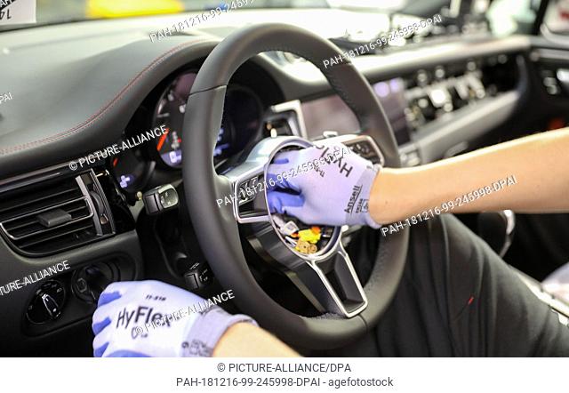 13 December 2018, Saxony, Leipzig: An employee assembles the steering wheel in a Porsche Macan at the Leipzig plant. The carmaker announced that the next...