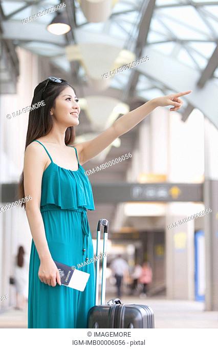 Young woman holding passport and airplane ticket with smile and pointing away