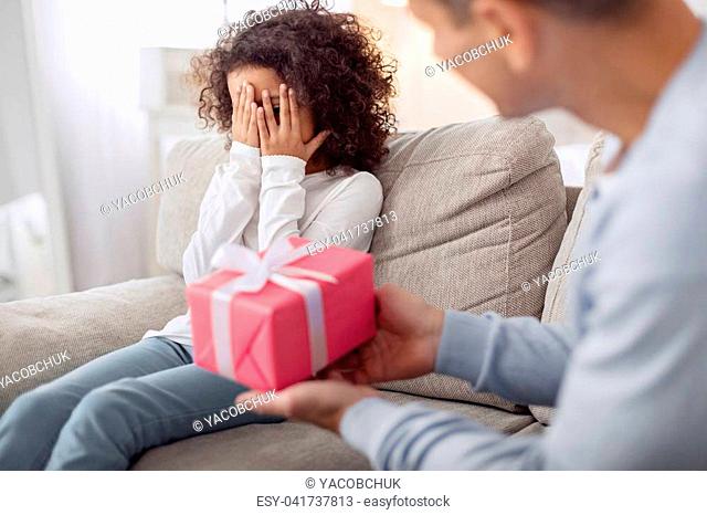 My gift. Inspired lovely curly-haired girl sitting on the sofa and closing her and her daddy holding a gift