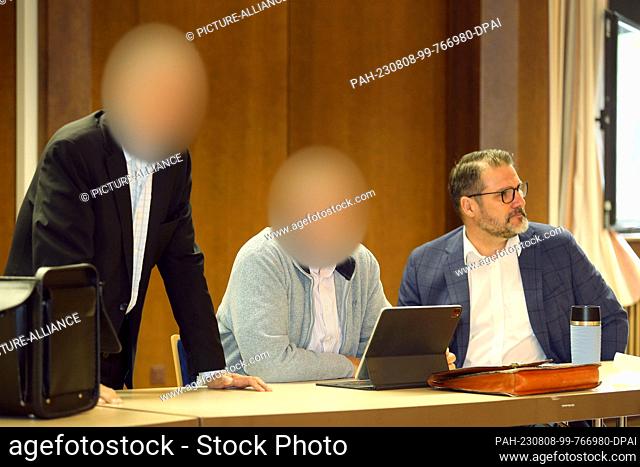 08 August 2023, Lower Saxony, Bovenden: Two defendants (l and M) in a trial for million-dollar renewable energy fraud stand and sit with a defense attorney in...