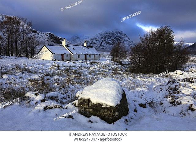 Black Rock Cottage on Rannoch Moor in the Scottish Highlands illuminated by the first rays of sunlight following an overnight snowfall in early November