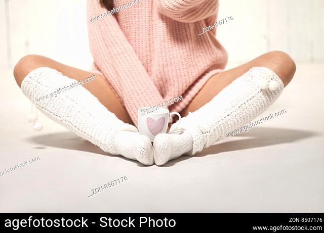 Girl with warm socks and sweater sitting on the floor with cup of coffee, hot chocolate or tea