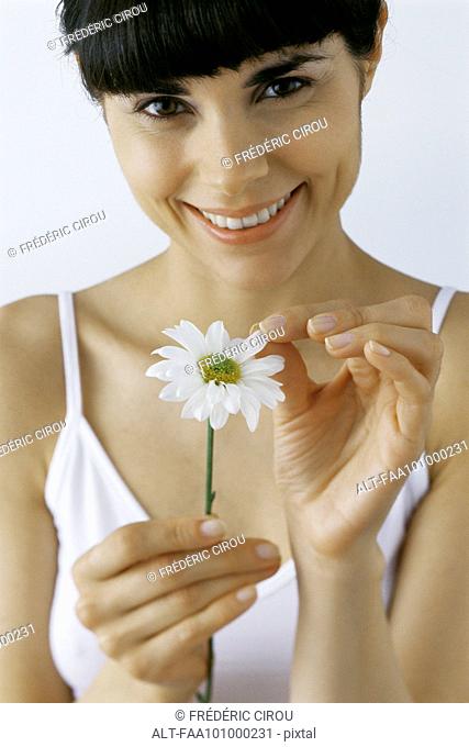 Young woman plucking petals from flower, smiling, portrait