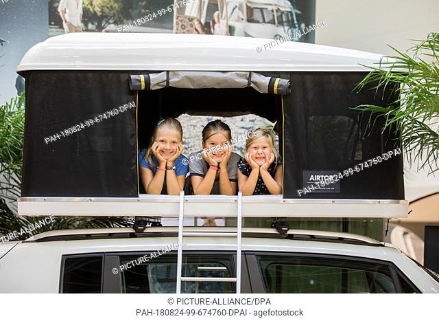 24 August 2018, Germany, Düsseldorf: Mathilde (l-r), Lucie and Lara are lying in a roof tent on a car of Autohome. The world's largest camping fair Caravan...