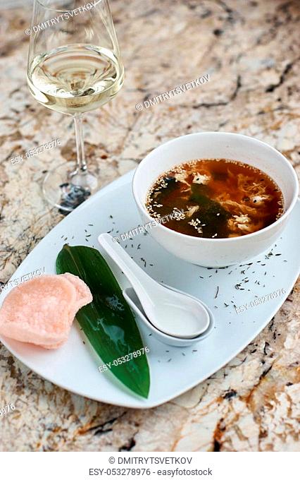 Crab soup served in white ceramic bowl with spoon, green leaf. pink crab chips and glass of white wine