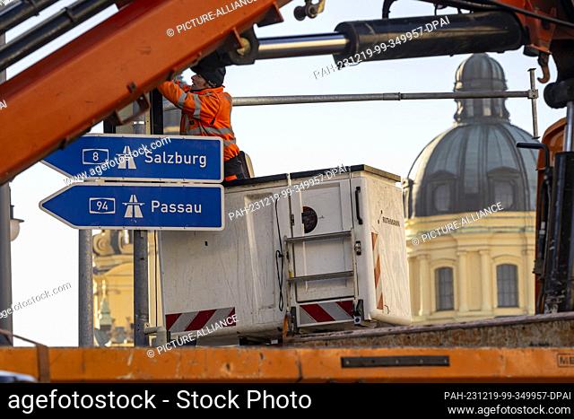 19 December 2023, Bavaria, Munich: A man in a lifting platform is laying cable harnesses for the traffic light control system across Ludwigstrasse near...