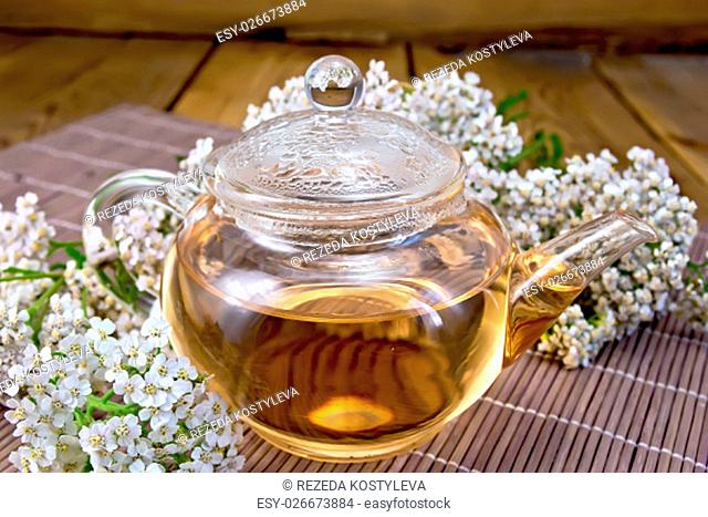 Tea with yarrow in a glass teapot, fresh flowers, yarrow on background of bamboo towels and wooden boards