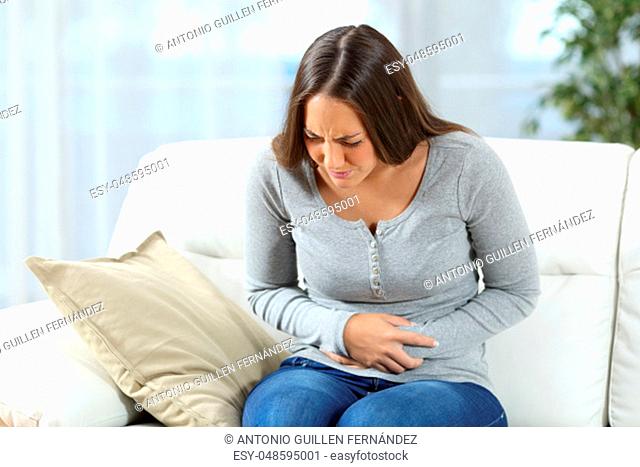 Woman suffering stomach ache and complaining sitting on a couch in the living room at home