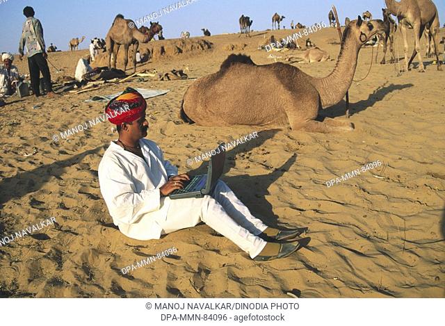 South Asian Indian rajput man using laptop for sending e-mail in desert at pushkar fair , rajasthan , India