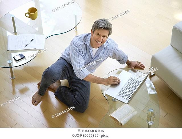 Man in living room sitting on floor using laptop