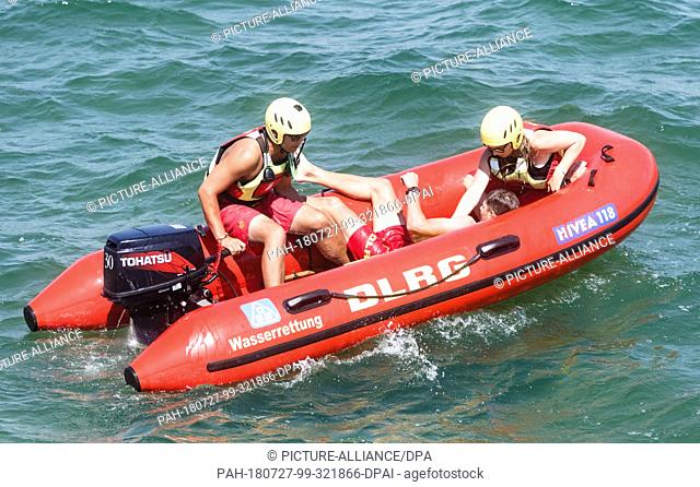 27.07.2018, Schleswig-Holstein, Scharbeutz: Two lifeguards of the German Lifesaving Society (DLRG) take the target person on board their inflatable boat during...