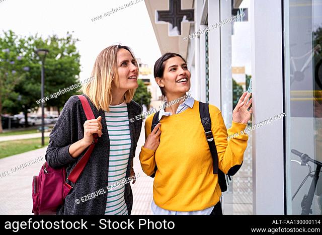 Photo of two female friends looking at shop windows and having a good time together