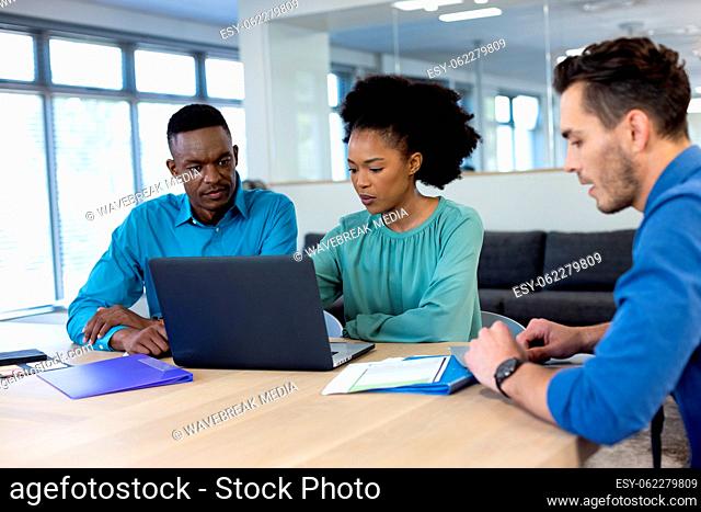 Happy diverse business people using laptop and discussing in modern office