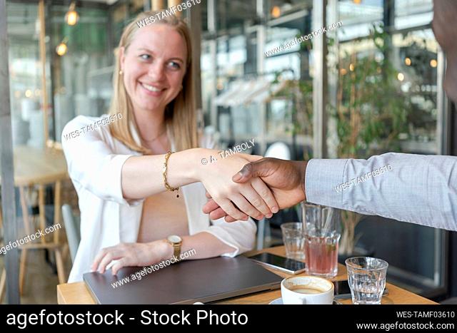 Happy businesswoman shaking hands with colleague in cafe