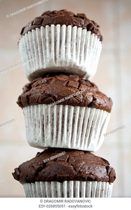 Three chocolate cupcakes stacked to form a tower in the kitchen