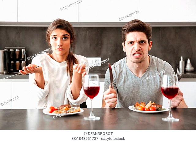 Portrait of an angry young couple sitting at the kitchen table and having dinner