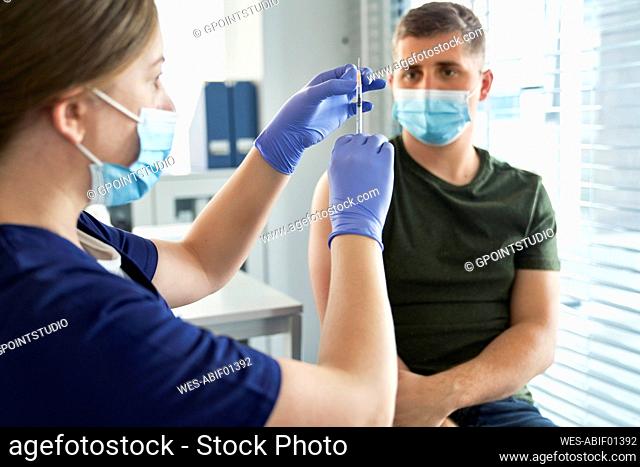 Female healthcare worker preparing vaccine syringe for male patient at center