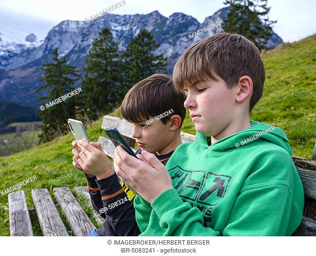 Two boys in nature are immersed in their smartphone, Ramsau, Berchtesgadener Land, Bavaria, Germany, Europe