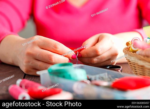 Woman sews red heart shaped toy by needle, conceptual symbol of love