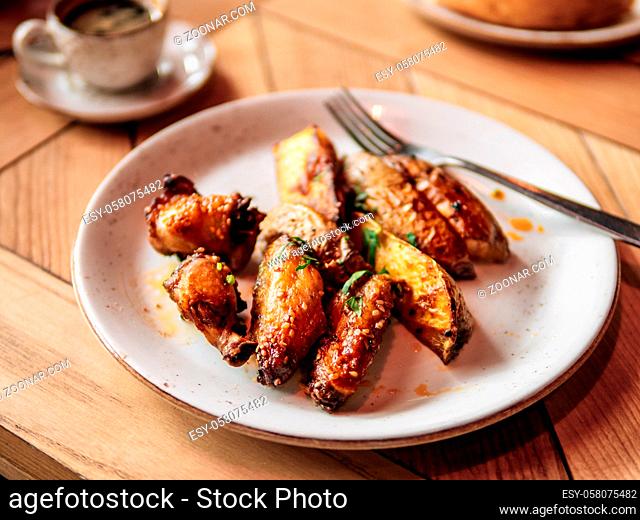 Tasty roasted chicken wings and roasted potatoes. Authentic shot of plate with roasted chicken wings and roasted potatoes on rustic wooden tabletop