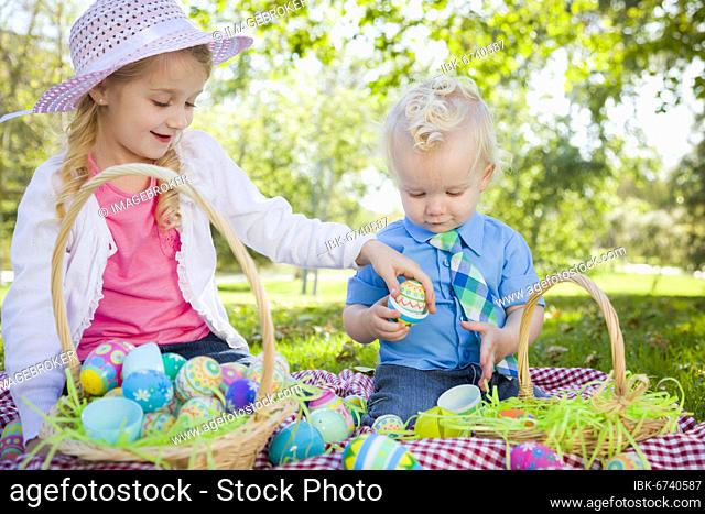 Cute young brother and sister enjoying their easter eggs outside in the park together