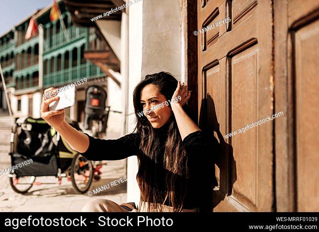 Smiling woman taking selfie while sitting by door
