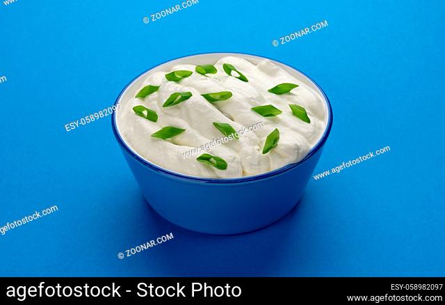 Bowl of sour cream with onion on blue background