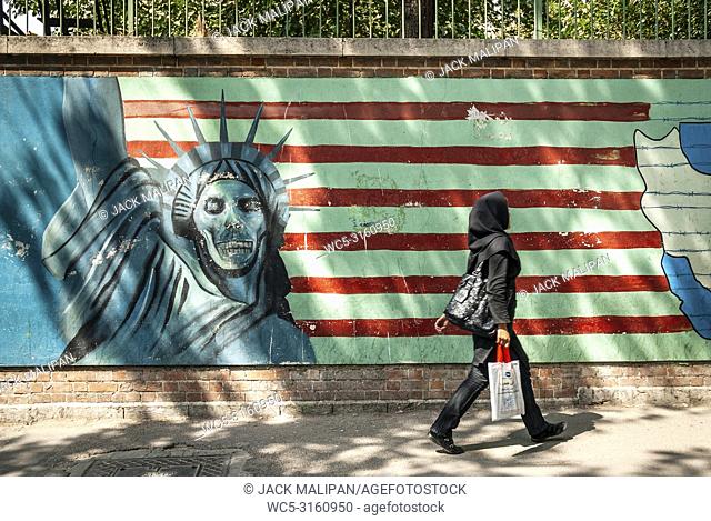 veiled muslim woman walking by anti american and israel propaganda mural on tehran street iran outside former US embassy