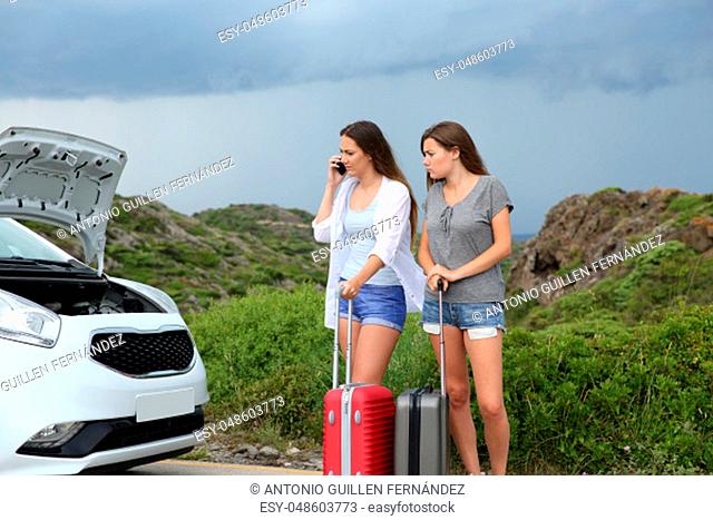 Frustrated tourists calling insurance about a brokendown car looking at the opened hood