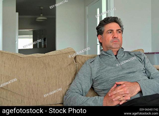 Upset mature adult man (male age 40-50) sitting on a couch alone with puzzled face expression