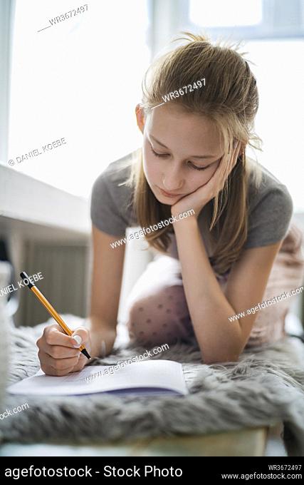 Girl learning at home, writing in exercise book