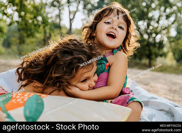 Cute sisters embracing each other at beach during vacation on sunny day