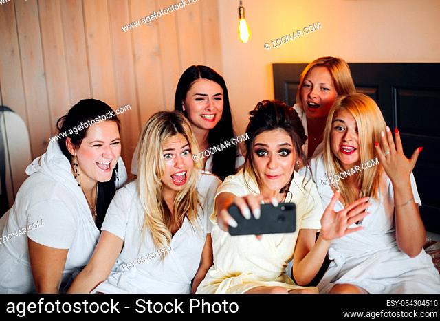 Group of pretty ladies with a bride in the middle in white taking selfie. They are having a hen party in a hotel or relaxing in spa