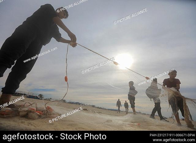 17 December 2023, Palestinian Territories, Rafah: Palestinian children hold a fishing net, as fishermen go fishing, taking a risk to feed their families as...