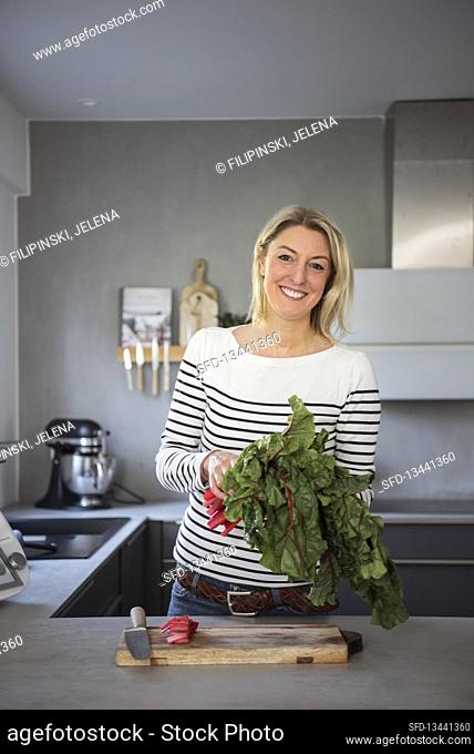Blonde woman with a bunch of rhubarb in a kitchen