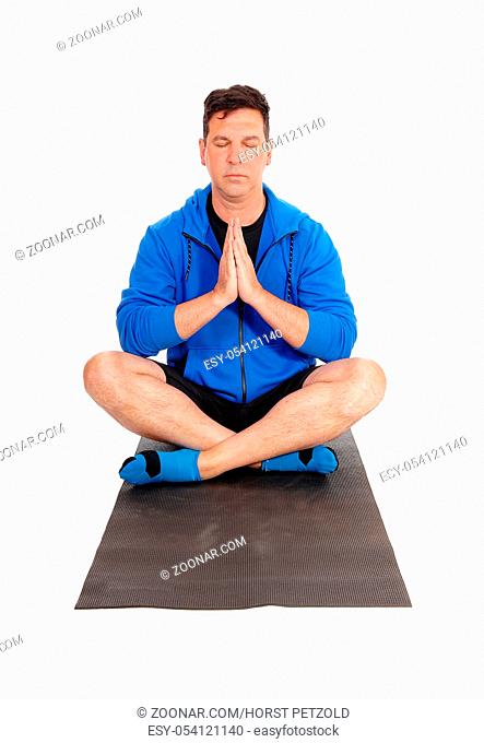 A meditating man in a blue jacket sitting on the floor in a yoga pose with his eyes closed and hand folded, isolated for white background