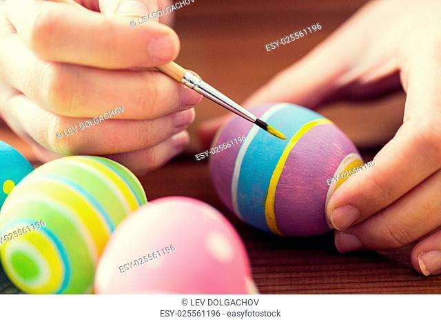 easter, holidays, tradition and people concept - close up of woman hands coloring easter eggs with brush