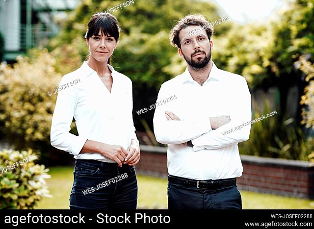 Confident businessman with arms crossed standing with female colleague