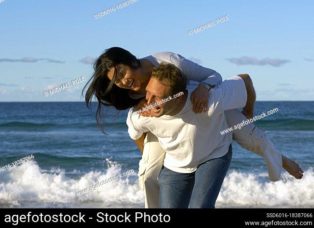 Man piggy backing woman along beach and laughing