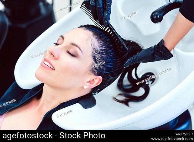 Artisan hairdresser diligently washing hair of customer woman