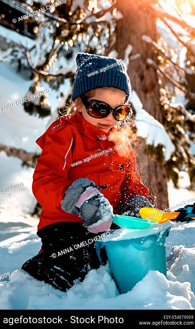 Little girl enjoying winter holidays, pretty child dressed in warm clothes and sunglasses having fun outdoors on backyard and playing with snow